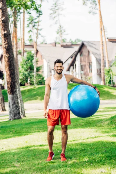 Deportista feliz de pie sobre hierba verde y la celebración de la pelota de fitness azul - foto de stock