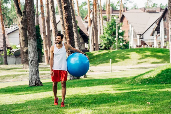 Deportista feliz caminando sobre hierba verde y sosteniendo la pelota de fitness - foto de stock
