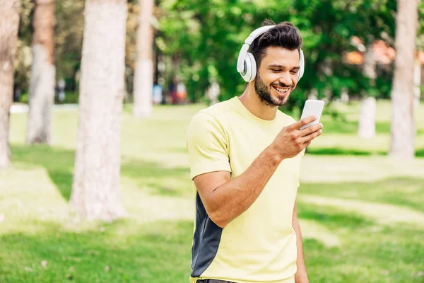 Hombre barbudo feliz mirando el teléfono inteligente y escuchando música - foto de stock