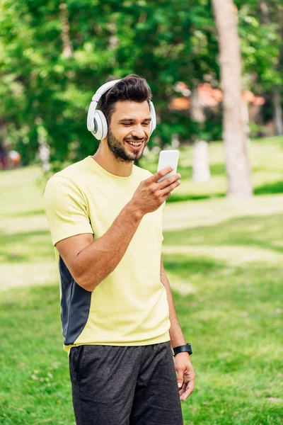 Homme barbu heureux regardant smartphone et écouter de la musique dans les écouteurs — Photo de stock