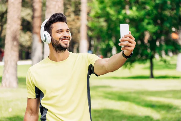 Happy bearded man taking selfie while holding smartphone and listening music in headphones — Stock Photo