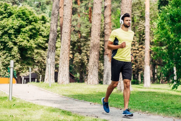 Bel homme barbu courir tout en écoutant de la musique dans les écouteurs dans le parc — Photo de stock