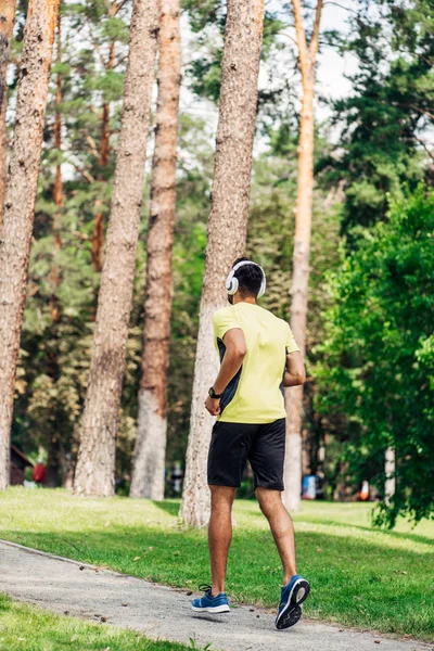Vista trasera del hombre corriendo mientras escucha música en auriculares en el parque - foto de stock