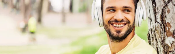 Tiro panorâmico de homem barbudo alegre ouvindo música em fones de ouvido — Fotografia de Stock