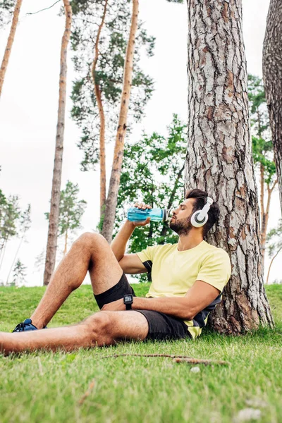 Enfoque selectivo del hombre con los ojos cerrados beber agua cerca de los árboles - foto de stock