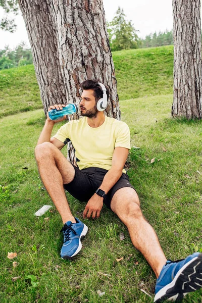 Selektiver Fokus eines gutaussehenden Mannes, der Wasser in der Nähe von Bäumen trinkt — Stockfoto