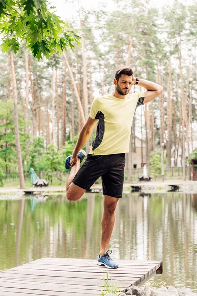 Hombre atlético en ropa deportiva haciendo ejercicio cerca del lago en el bosque - foto de stock