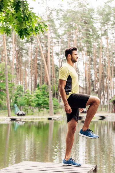 Uomo bello e atletico in abbigliamento sportivo esercizio vicino al lago — Foto stock
