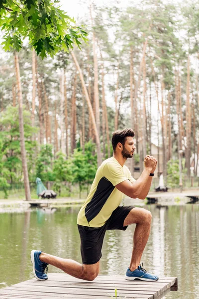 Handsome and athletic man in sportswear exercising near lake in forest — Stock Photo