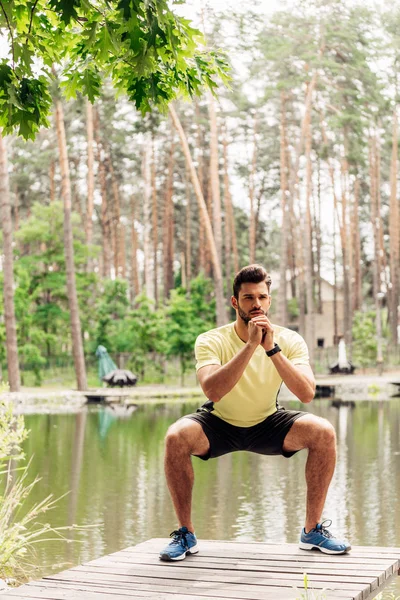 Handsome man in sportswear exercising near lake in forest — Stock Photo