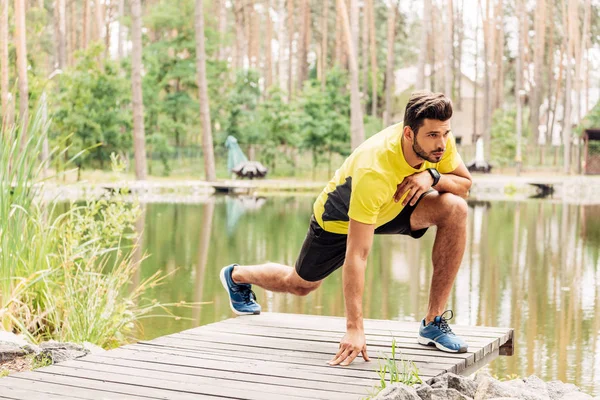 Bel homme barbu en tenue de sport faisant de l'exercice près du lac en forêt — Photo de stock