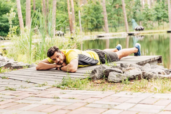 Вибірковий фокус спортсмена в спортивному одязі, що лежить біля озера в лісі — стокове фото