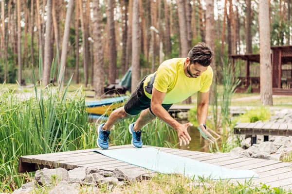 Bärtiger Mann in Sportbekleidung trainiert auf Fitnessmatte in der Nähe von Steinen und Bäumen — Stockfoto