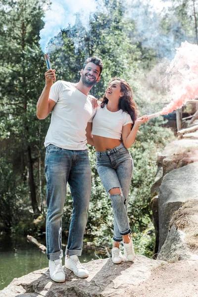 Happy bearded man and attractive woman holding smoke bombs — Stock Photo