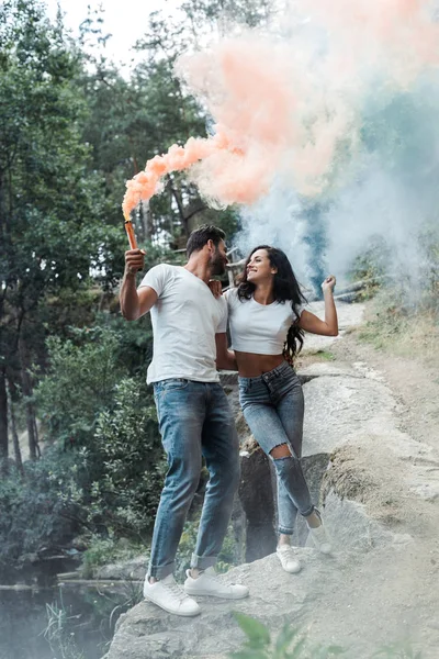 Mujer positiva y hombre barbudo alegre sosteniendo bombas de humo - foto de stock