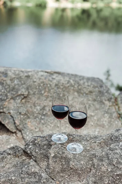 Selective focus of wine glasses with red aromatic wine on stone near lake — Stock Photo