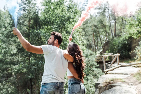 Low angle view of woman and bearded man holding smoke bombs — Stock Photo