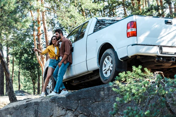 Baixo ângulo vista de mulher feliz de pé perto barbudo homem e carro na floresta — Fotografia de Stock