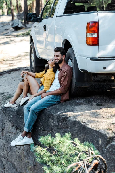 Hombre barbudo feliz y atractiva mujer sentada cerca del coche - foto de stock