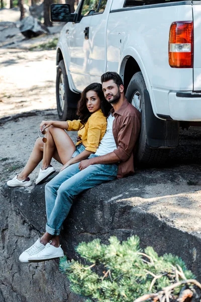 Schöner und bärtiger Mann sitzt neben Auto mit attraktiver Frau — Stockfoto