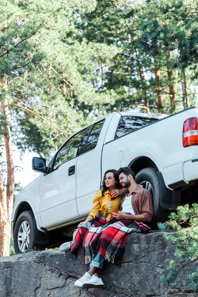 Hombre guapo y chica atractiva en gafas de sol sosteniendo tazas cerca del coche - foto de stock