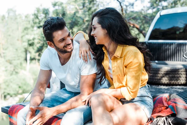 Hombre barbudo alegre mirando a la mujer bonita sentada en manta a cuadros - foto de stock