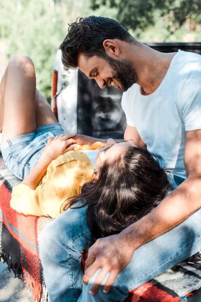 Schöner bärtiger Mann lächelt, während er Mädchen ansieht, die auf karierter Decke liegen — Stockfoto