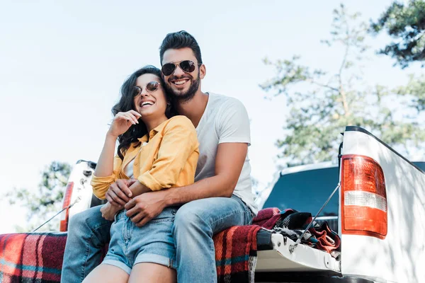 Vista basso angolo di allegro uomo barbuto abbracciare donna in occhiali da sole — Foto stock