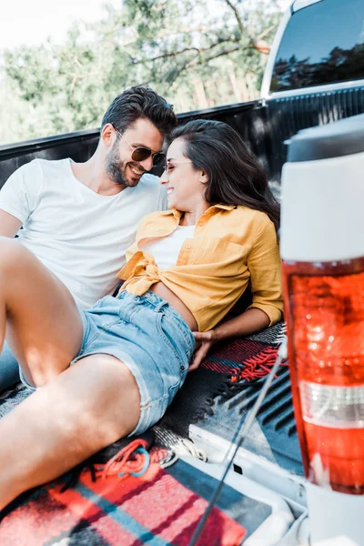 Selective focus of bearded man looking at young and happy woman lying on blanket in summertime — Stock Photo