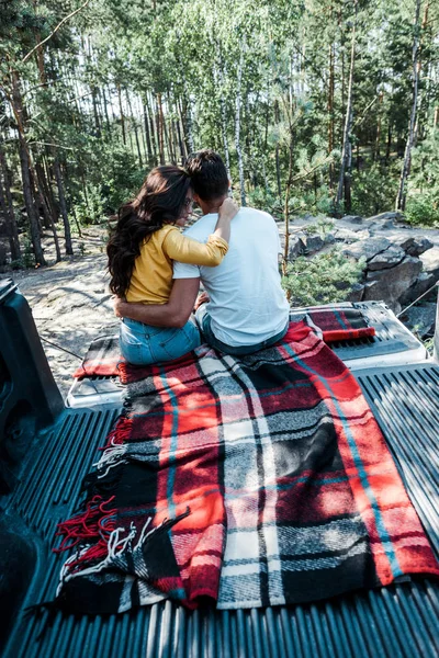 Rückansicht einer Frau und eines Mannes, die sich im Kofferraum eines Autos im Wald umarmen — Stockfoto