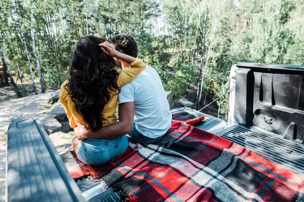 Vue arrière de l'homme étreignant femme tout en étant assis dans le coffre de la voiture dans les bois — Photo de stock