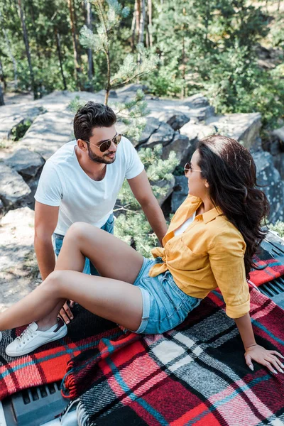 Bello uomo in occhiali da sole guardando la donna mentre seduto in auto tronco nel bosco — Foto stock