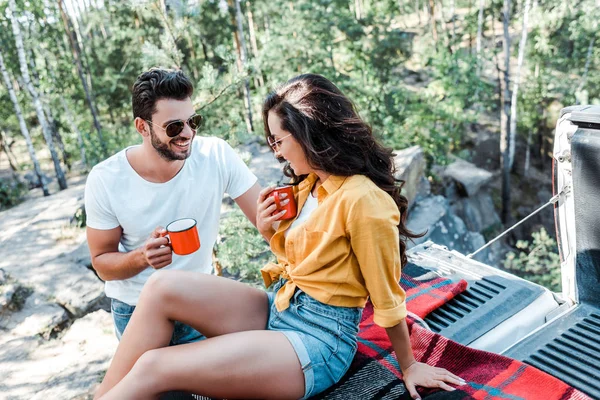 Hombre feliz en gafas de sol y chica alegre sosteniendo tazas - foto de stock