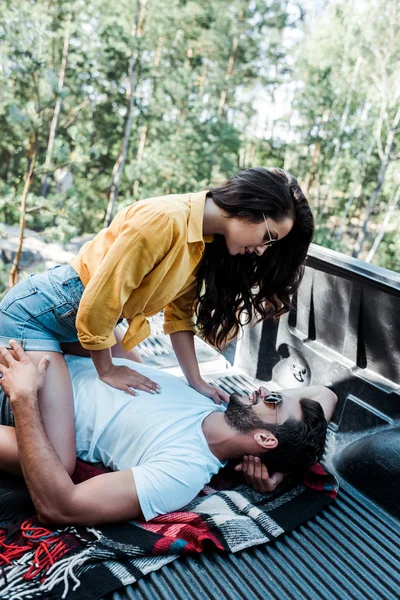 Chica atractiva en gafas de sol mirando hombre guapo acostado en manta - foto de stock