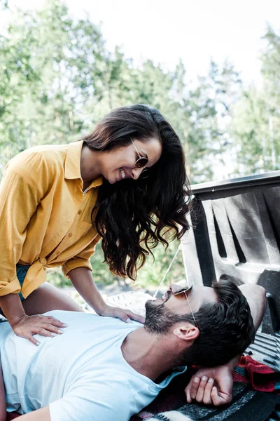 Happy girl in sunglasses looking at handsome man lying on blanket — Stock Photo