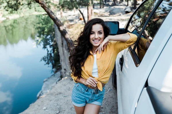 Selektiver Fokus glücklicher Mädchen, die lächeln, während sie in der Nähe von Auto im Wald stehen — Stockfoto