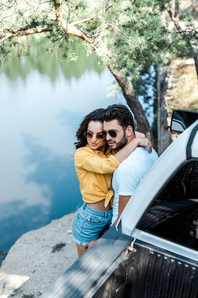 Vista aérea de la mujer abrazando novio cerca de automóvil y lago - foto de stock