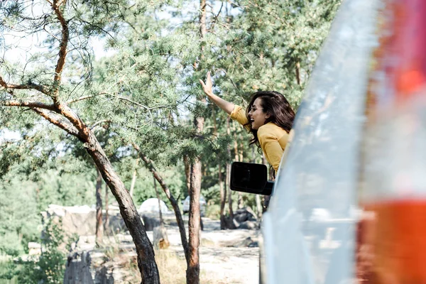 Вибірковий фокус весела дівчина махає рукою з вікна автомобіля в лісі — стокове фото