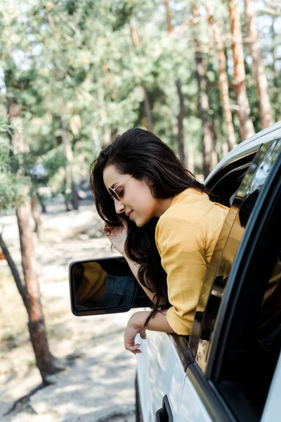 Selektiver Fokus des fröhlichen Mädchens, das aus dem Autofenster im Wald lächelt — Stockfoto