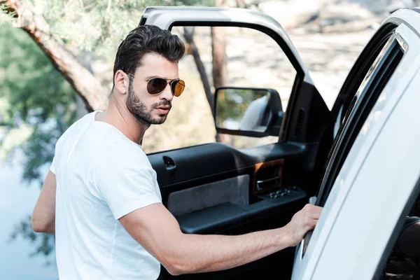 Enfoque selectivo del hombre barbudo en gafas de sol de pie cerca del coche - foto de stock