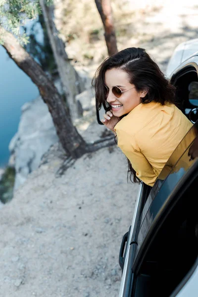 Vista aérea de chica alegre sonriendo desde la ventana del coche en el bosque - foto de stock