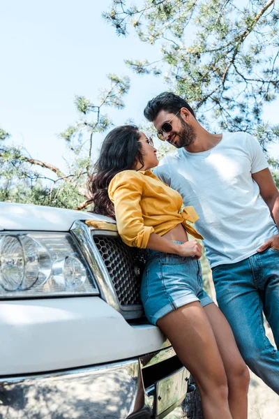 Low angle view of handsome man looking at woman near auto in woods — Stock Photo