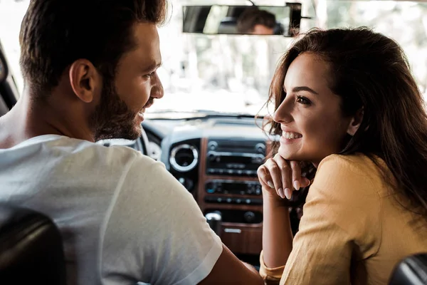 Vista lateral del hombre feliz mirando a la mujer alegre en coche - foto de stock