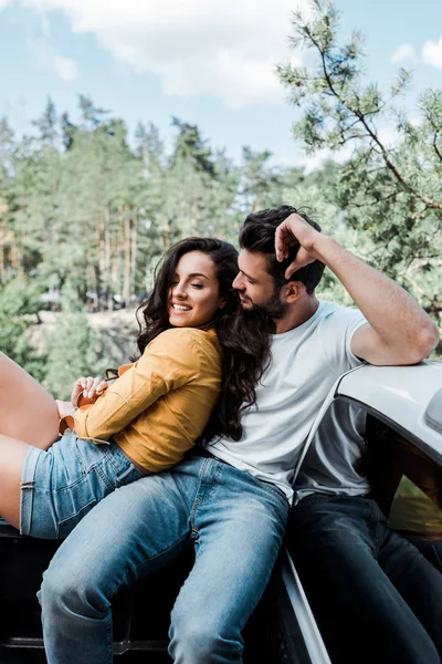 Barbudo hombre sentado y mirando feliz chica en el bosque - foto de stock