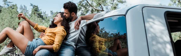 Panoramic shot of bearded man sitting and looking at happy girl in woods — Stock Photo