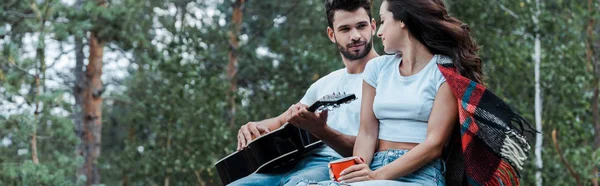 Панорамний знімок людини, що тримає акустичну гітару і дивиться на дівчину — стокове фото