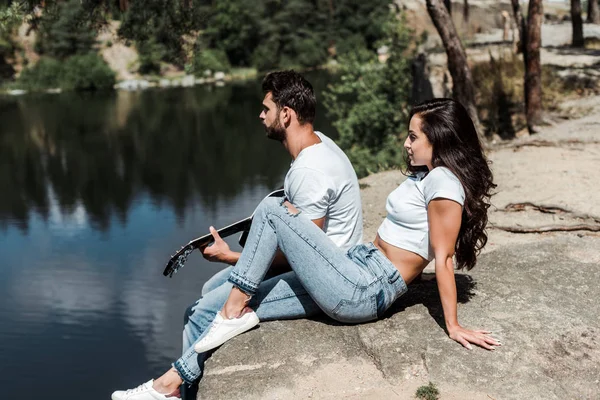 Bel homme jouant de la guitare acoustique près de la jeune femme — Photo de stock