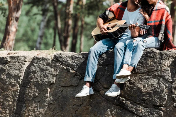 Обрезанный вид мужчины, играющего на акустической гитаре рядом с молодой женщиной, завернутой в одеяло — стоковое фото