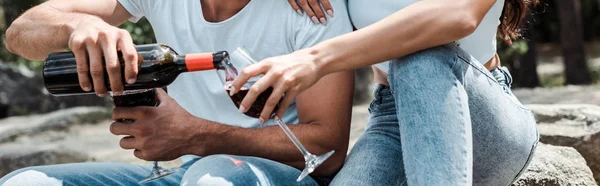 Panoramic shot of man pouring red wine from bottle near woman — Stock Photo