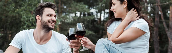 Tiro panorámico de hombre feliz y joven tintineo copas de vino - foto de stock